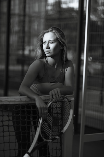 Erstaunliche blonde Frau mit perfektem Körper, die mit einem Tennisschläger auf dem Platz posiert. Monochrome Tönung