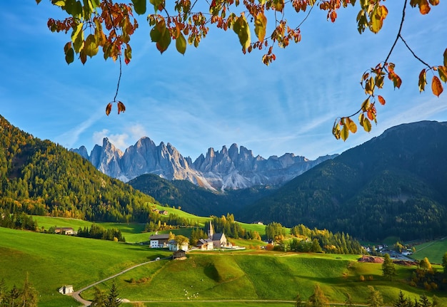 Erstaunliche Herbstlandschaft im Dorf Santa Maddalena mit bunten Kirchenbäumen und Wiesen unter aufgehenden Sonnenstrahlen Dolomiten Italien