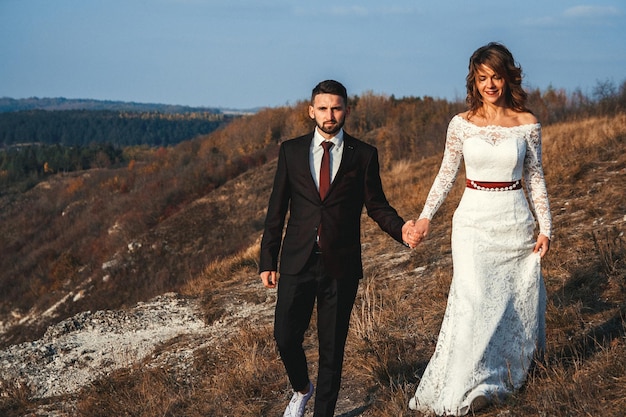 Erstaunliche Hochzeitspaarbraut und -bräutigam, die Händchen auf einem Berg- und Flusshintergrund halten