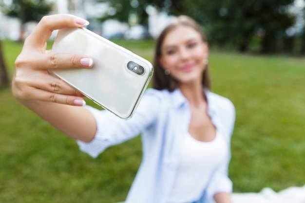 Erstaunliche junge hübsche Frau im Park im Freien macht ein Selfie mit dem Handy.