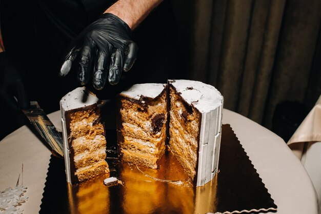 Erstaunliche Kuchen. Ein Koch mit schwarzen Handschuhen schneidet eine Schokoladenhochzeitstorte. Die Hochzeitstorte ist innen auf einer schwarzen Oberfläche köstlich. Großer Kuchen in weißer Schokolade.