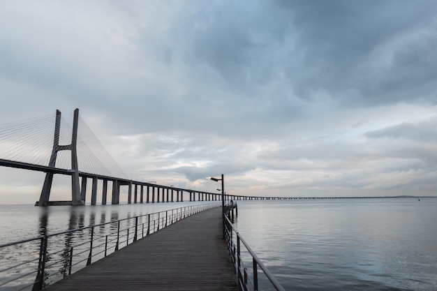 Erstaunliche lange Brücke Vasque da Gama mit Holzsteg Meer und Wolken in Lissabon Portugal