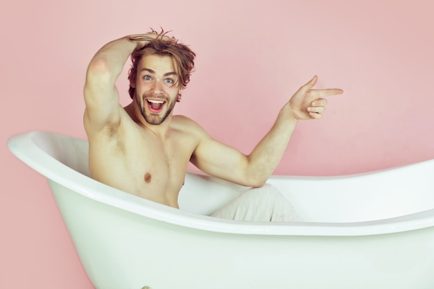 Erstaunlicher sexy mann mit muskulösem körper, der im weißen badewannenmann-spa und im schönheits-entspannungs- und hygiene-gesundheitskopierraum sitzt