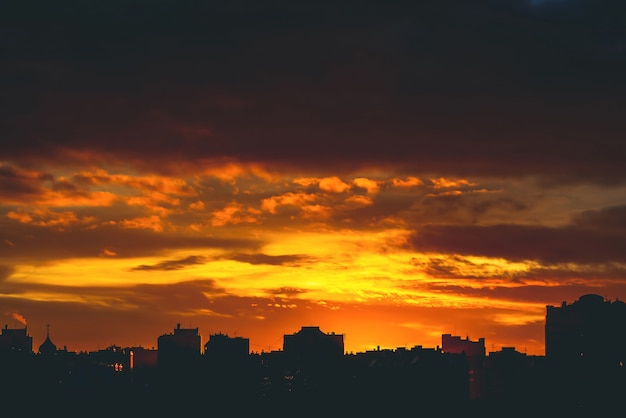 Erstaunlicher warmer drastischer bewölkter Himmel über dunklen Schattenbildern von Stadtgebäuden.