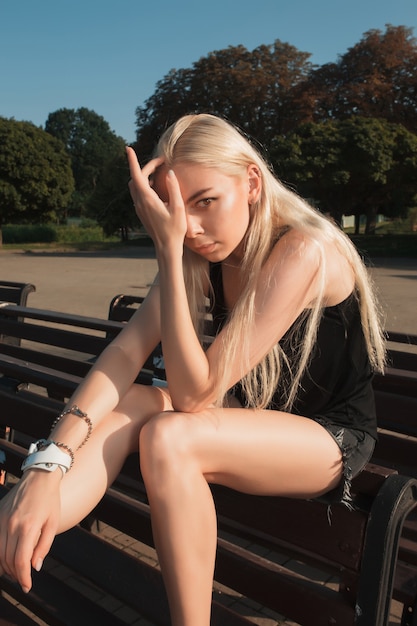 Erstaunliches blondes Model mit langen Haaren, das Freizeitkleidung trägt und im Park posiert
