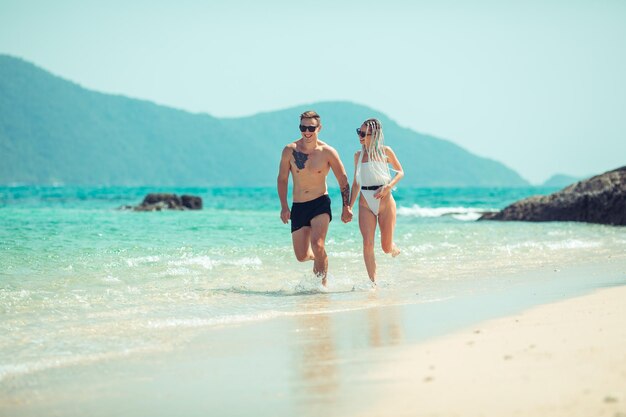 Erstaunliches junges Paar läuft Hand in Hand am Strand, der Mann in Badehose und seine Freundin