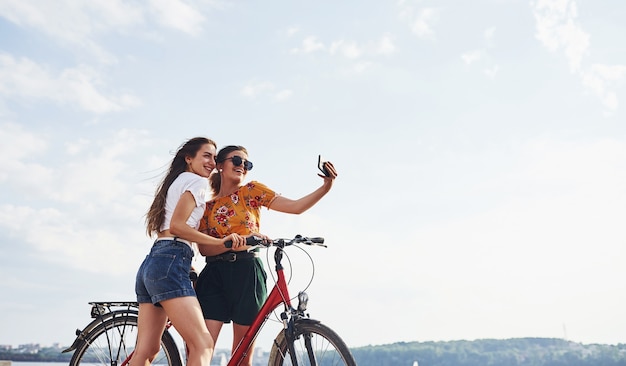 Erstaunliches Selfie machen. Zwei Freundinnen auf dem Fahrrad haben Spaß am Strand in der Nähe des Sees.