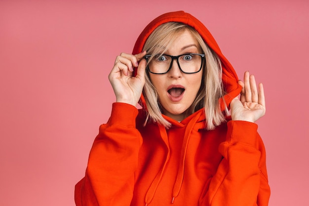 Erstaunt schockiert überraschte junge blonde Frau, die isoliert auf rosa Hintergrund in die Kamera schaut.