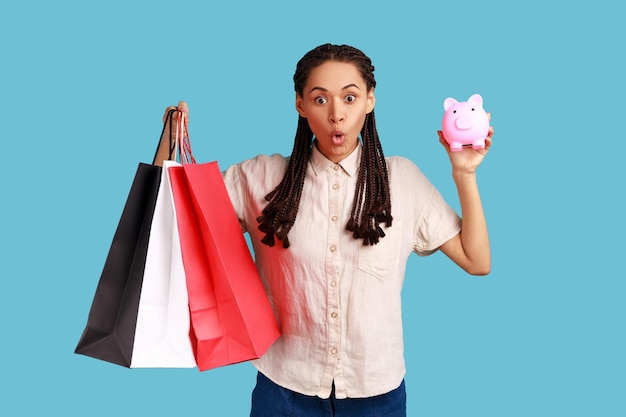 Erstaunte Frau, die Einkaufstaschen und Sparschwein-Cashback vom Kauf von Einkäufen hält