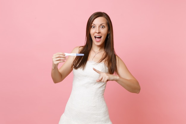 Erstaunte Frau im weißen Kleid, die mit dem Zeigefinger auf den Schwangerschaftstest in der Hand zeigt