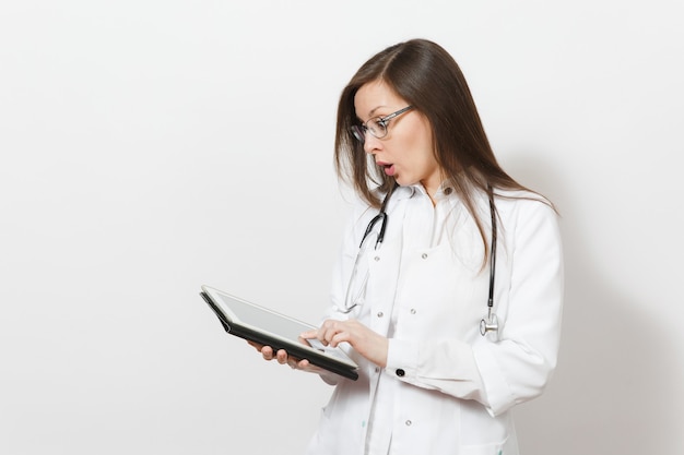 Erstaunte hübsche junge Doktorfrau mit Stethoskop, Brille isoliert auf weißem Hintergrund. Ärztin im medizinischen Kittel mit Tablet-PC-Computer. Personal im Gesundheitswesen, Konzept der Technologiemedizin.