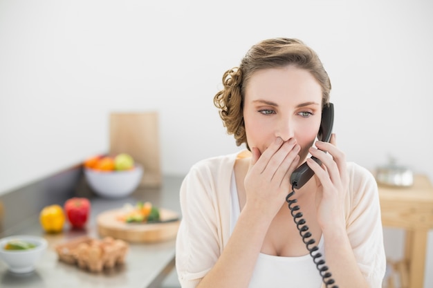 Erstaunte junge Frau, die mit ihrem Telefon in ihrer Küche anruft