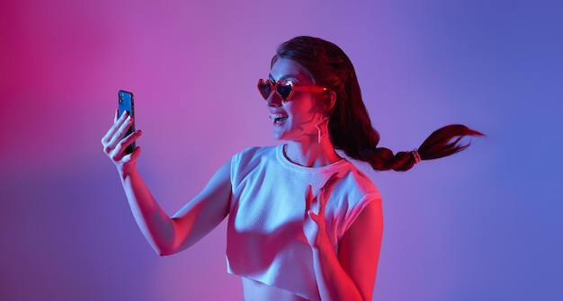 Erstaunte junge Frau mit Handy auf Neon-Hintergrund digitale Medientechnologie 5g-Konzept
