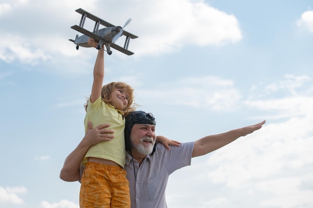 Erstauntes Enkelkind und Großvater, die Spaß mit dem Flugzeug im Freien auf Himmelshintergrund mit Kopienraum haben