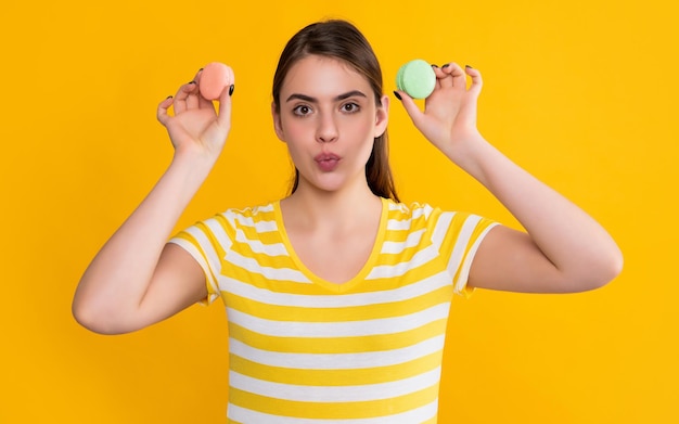 Erstauntes junges Mädchen mit Macaron auf gelbem Hintergrund