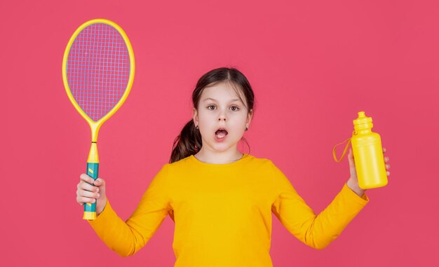 Erstauntes Kind hält Tennisschläger und Wasserflasche auf rosa Hintergrund