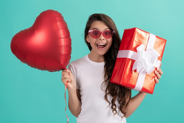 Erstauntes Kind in Brillen hält Geschenkbox und Valentinstag-Party-Herzballon, Liebestag.