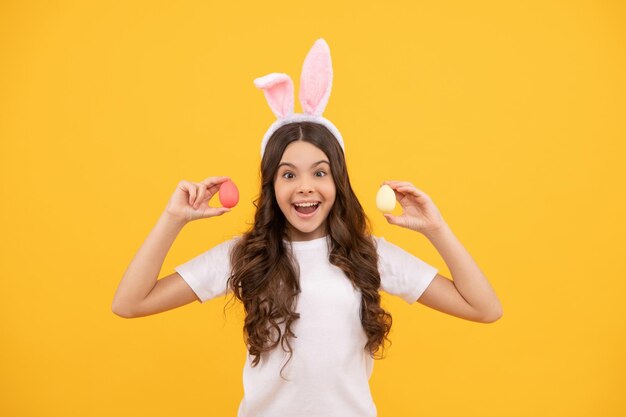 Erstauntes Kind in Hasenohren hält Eier auf gelbem Hintergrund, frohe Ostern