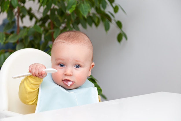 Erste Fütterung des Jungen, essen Joghurt, schmutzigen Mund, hält Löffel