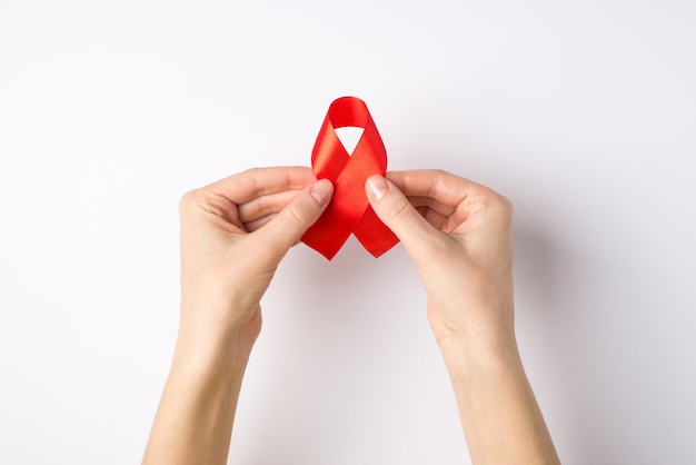 Erste-Person-Draufsicht-Foto von Mädchenhänden mit rotem Seidenband-Symbol des Aids-Bewusstseins auf isoliertem weißem Hintergrund mit Copyspace