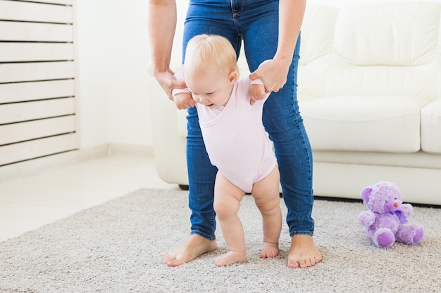 Erste Schritte des Baby-Kleinkindes, das im weißen, sonnigen Wohnzimmer laufen lernt. Schuhe für Kinder.