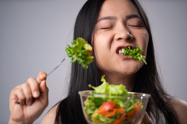 Erster Eindruck asiatische Frau, die Salat lokalisiert über weißer Wand isst. Gesunder Lebensstil mit Clean Food-Konzept.