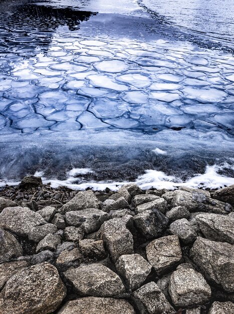 Erster Frost des Gefriersees in Form von kleinen Eiswürfeln und großen Steinen an der Uferlandschaft