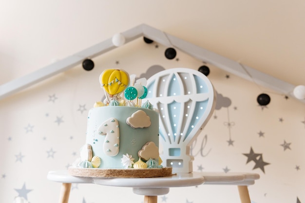 Erster Geburtstagskuchen für Kinder Blauer Kuchen mit Wolken Baiser und Luftballons auf dem Hintergrund der Kinderzimmerbeleuchtung