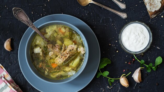 Erster Kurs. Hühnersuppe und Sauerrahmsauce auf einem dunklen Tisch