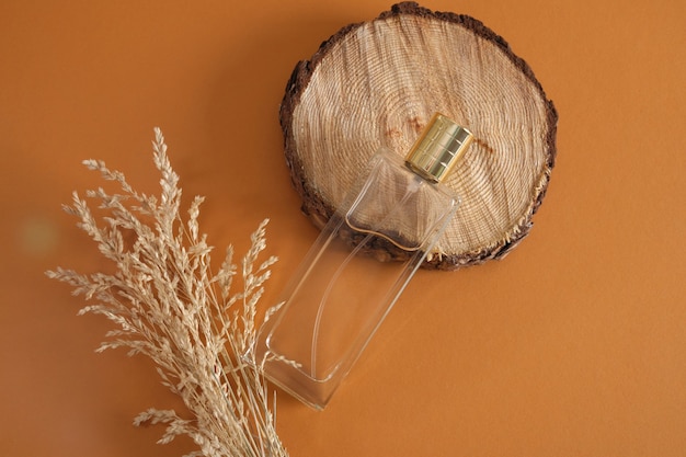 Erva seca e um frasco retangular de perfume com uma tampa dourada em uma serra redonda, corte de um pódio de árvore em um fundo marrom