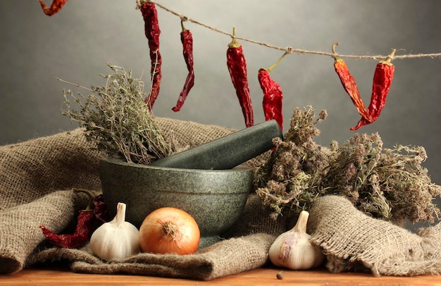 Ervas secas em argamassa e legumes na mesa de madeira no fundo cinza