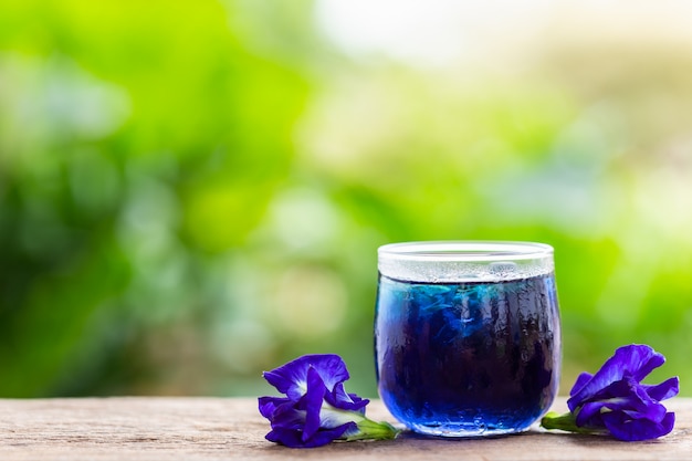 Ervilha de borboleta roxa fresca ou flor de ervilha azul e suco em vidro no fundo da mesa de madeira