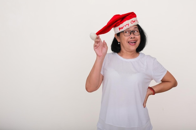 Erwachsene asiatische Frau steht und lächelt mit Weihnachtsmannshut, bereit, Weihnachten zu feiern