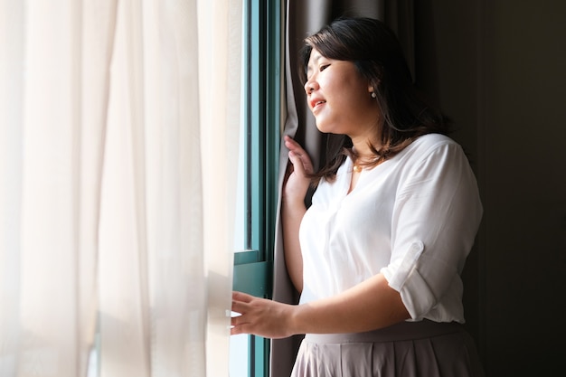 Erwachsene asiatische Frauen, die glücklich lächeln, während sie durch das Fenster schauen