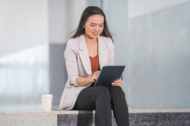 Erwachsene asiatische Geschäftsfrau mit digitalem Tablet-Computer und im Büro im Freien arbeiten