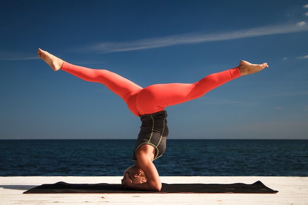 Erwachsene blonde Frau mit kurzem Haarschnitt übt Yoga auf dem Pier