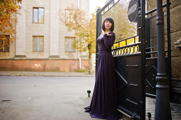 Erwachsene Brünette Frau am violetten Kleid Hintergrund schwarze Eisentore