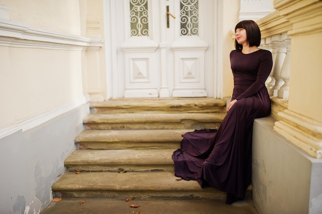 Erwachsene brünette Frau im violetten Kleid Hintergrund altes Vintage-Haus mit Treppe