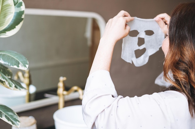 Erwachsene brünette Frau mit Blattmaske im Gesicht im Badezimmer zu Hause