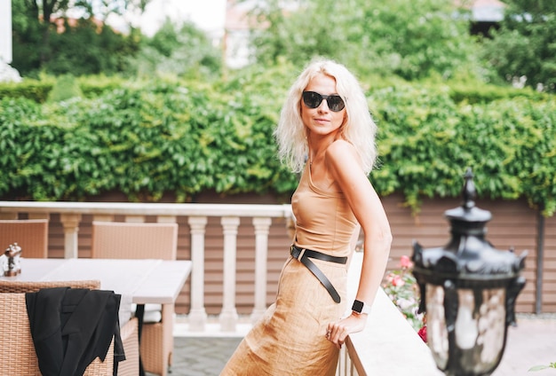 Erwachsene elegante blonde Frau in beigefarbener Kleidung der Sonnenbrille im Straßencafé der Sommerstadt