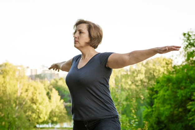 Erwachsene Frau, die Übungen am See im Park an einem Sommertag tut