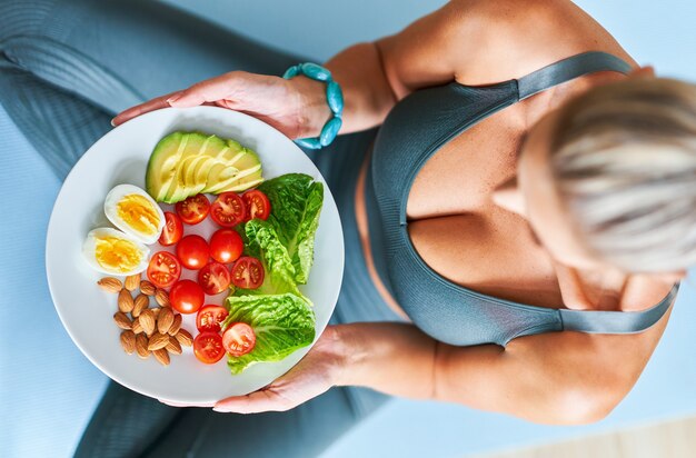 erwachsene Frau, die gesundes Mittagessen isst und auf Yogamatte sitzt