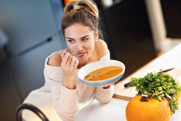 Erwachsene Frau, die in der Küche Kürbissuppe schmeckt