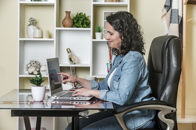 Erwachsene Frau, die Laptop mit Vergnügen in der hellen zeitgenössischen Wohnung verwendet