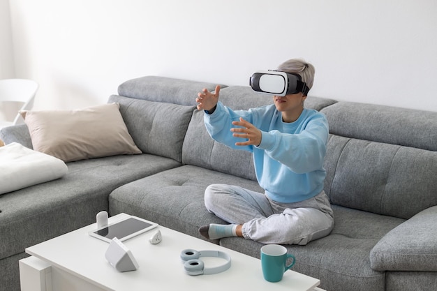 Erwachsene Frau, die Videospiele mit einem VR-Headset spielt, während sie auf dem Sofa sitzt