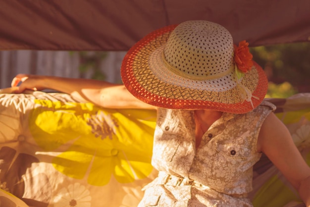 Erwachsene Frau mit Sommerhut sitzt auf einer Schaukel im Hof