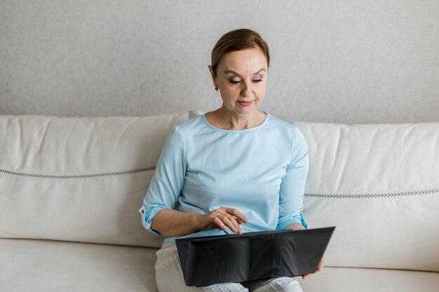 Erwachsene Frau sitzt auf der Couch auf ihrem Schoß sie hat einen schwarzen Laptop drauf sie arbeitet