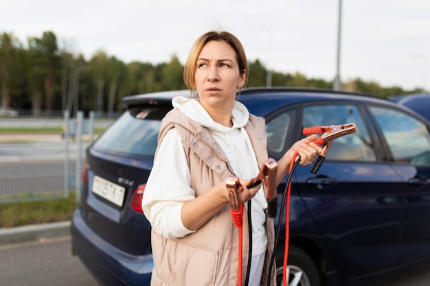Erwachsene Frau steht Autoinstallateur mit Kabeln, um Batterie aufzuladen