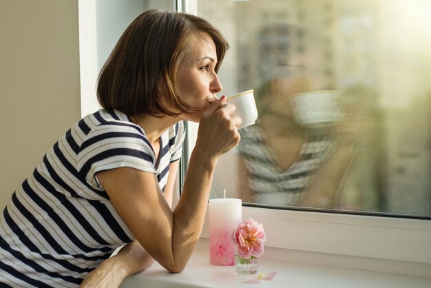 Erwachsene Frau trinkt Kaffee, schaut aus dem Fenster