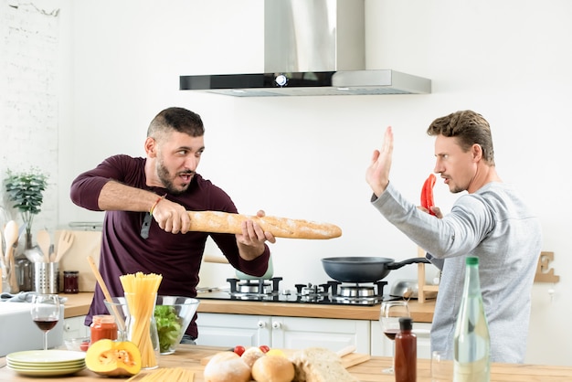 Erwachsene homosexuelle männliche Paare, die herum mit Lebensmittelinhaltsstoffen in der Küche spielen